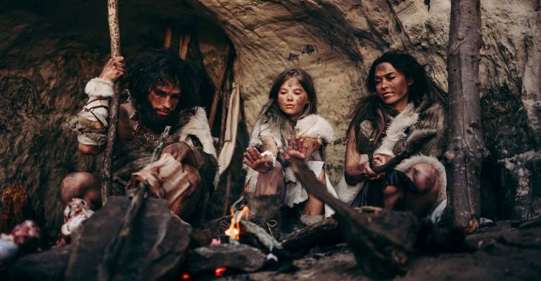 Three prehistoric women sitting around a fire inside a cave.